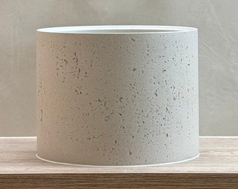 Op de afbeelding: Een witte betonnen wastafel met een getextureerd oppervlak. De wastafel is gemonteerd op een houten aanrechtblad. Er zijn drie zwarte armaturen aan de muur achter de wastafel, waaronder een kraan.
