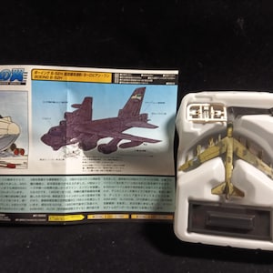 May include: A model airplane in a white plastic tray, with a detailed illustration of the Boeing B-52H on a printed sheet. The model is olive green and brown. The sheet has Japanese text.