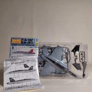 May include: A model kit of an F/A-18F EA-18G Super Hornet Growler aircraft. The kit includes a gray plastic model in a clear plastic tray, along with instruction sheets. The box art features images of the aircraft.