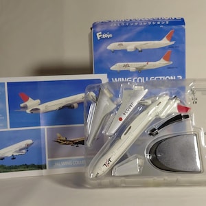 May include: A white and red model aeroplane, partially assembled, with the text "JAL" and "JA8534" visible. The model is packaged in a clear plastic tray, with a box and informational card featuring images of the plane.