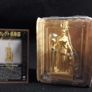 May include: A tan-colored figurine of a woman in a classical pose, packaged in a clear plastic container. The figurine is next to a card with Japanese text and a smaller image of the figurine. The figurine is of Athena.