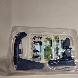 Op de afbeelding: Een modelvliegtuigkit met diverse donkerblauwe en groene plastic onderdelen. De kit bevat de romp, vleugels, staart en andere componenten, allemaal in een doorzichtige plastic tray. Het model is gedeeltelijk gemonteerd.