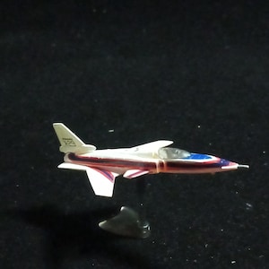 May include: A small toy airplane with a white body, red and blue accents, and a black cockpit. The wings and tail are white. The plane is on a black surface.