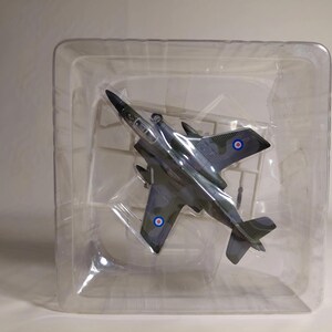 Puede incluir: Maqueta de avión con diseño de camuflaje en tonos grises y verdes, presentada en un envase de plástico transparente. El avión tiene alas y cola, y muestra escarapelas con círculos rojos, blancos y azules. Es una réplica en miniatura.