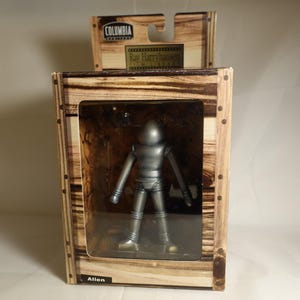 May include: A silver-colored alien figure in a wooden box with the text "Ray Harryhausen" and "Alien" on the box.