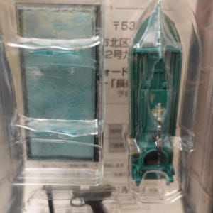 Puede incluir: Un barco de juguete verde en un paquete de plástico transparente. El barco tiene un diseño detallado con un pequeño emblema en la parte delantera. El paquete también contiene un artículo rectangular con una superficie de color turquesa.