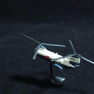 May include: A miniature model helicopter, predominantly white and navy blue, with a red circle emblem and the number "8604" visible. The model has two sets of rotating blades and is mounted on a small stand.