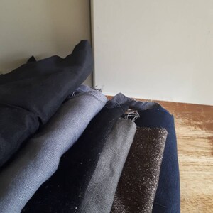 May include: A stack of fabric swatches in various shades of blue and grey, including a dark blue, a light grey, a dark grey, and a brown fabric with a subtle shimmer.