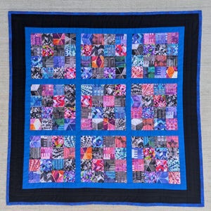 May include: A blue and black quilt with a geometric pattern. The quilt is made up of many small squares, each with a different pattern. The quilt is framed with a black border and a blue outer border.