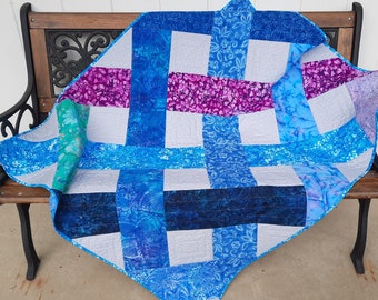 May include: A patchwork quilt with a woven pattern in shades of blue, purple, and white. The quilt is made of various fabrics with floral and abstract designs.