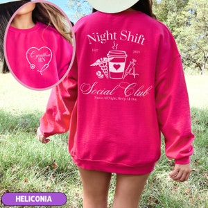 K&ouml;nnte beinhalten: Rosafarbener Pullover mit einem wei&szlig;en Grafikdesign, auf dem "Night Shift Social Club" mit einer Kaffeetasse, einem Stethoskop und einer Spritze steht. Der Text "EST 2024" befindet sich &uuml;ber dem Grafikdesign und der Text "Nurse All Night, Sleep All Day" darunter. Der Pullover hat auch ein wei&szlig;es Herz mit dem Text "Cynthia RN" auf der Vorderseite.