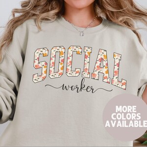 May include: A light beige sweatshirt with a floral print design. The text "SOCIAL worker" is printed on the front of the sweatshirt.