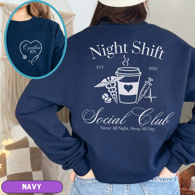 K&ouml;nnte beinhalten: Navyblauer Sweatshirt mit einer wei&szlig;en Grafik einer Kaffeetasse, einem Stethoskop, einer Pille und einer Spritze. Der Text "Night Shift Social Club" ist in einer kursiven Schrift geschrieben. Der Text "Nurse All Night, Sleep All Day" steht unter der Grafik. Der Text "EST 2024" steht &uuml;ber der Grafik.