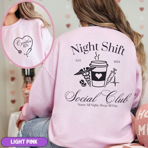 K&ouml;nnte beinhalten: Hellrosafarbener Pullover mit dem Text "Night Shift" und "Social Club" auf der R&uuml;ckseite. Das Design beinhaltet eine Kaffeetasse, ein Stethoskop, eine Spritze und ein Herz. Der Text "EST 2024" ist ebenfalls auf der R&uuml;ckseite aufgedruckt.