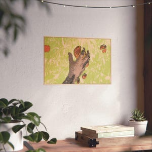 Puede incluir: Una impresión artística enmarcada que presenta una mano que alcanza varios objetos de color naranja. La obra de arte tiene un fondo verde y beige con una apariencia texturizada. El marco es de color marrón claro.