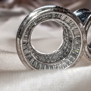 May include: A set of three silver rings with a circular design, each ring is adorned with a row of sparkling diamonds.