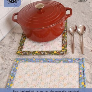 May include: A red, extra large, silicone trivet with a floral pattern. The trivet is 11 inches by 14 inches and includes instructions and a 9 inch by 12 inch silicone overlay.  The trivet is shown with a red pot on top.