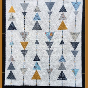 May include: A quilt pattern called "Sergeant Pepper" featuring a white background with rows of colorful triangles. The triangles are in shades of blue, gray, and yellow. The quilt is made by Abbey Lane Quilts and is numbered #205.