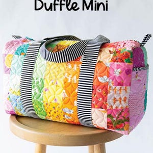 May include: A colorful patchwork mini duffel bag with black and white striped handles. The bag is made of quilted fabric and has a variety of floral and geometric patterns. The bag is sitting on a wooden stool. The text "Patchwork Duffle Mini" is displayed above the bag and "Knot + Thread Design" is displayed below the bag.