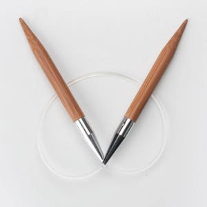 May include: A pair of wooden knitting needles with silver tips. The needles are crossed and resting on a white surface.