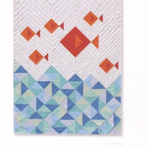May include: A quilt pattern featuring a design of orange fish swimming above a blue and green geometric pattern. The quilt is titled "little fishies quilt" and is by Whole Circle Studio.