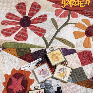 May include: A handmade quilt with large floral appliqués in red plaid and orange fabrics. The quilt features the text "Stellar Garden." Small framed pressed flower art and a vintage photograph are displayed on the quilt.