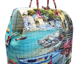 Könnte beinhalten: Eine große, gesteppte Tragetasche mit Blumenmuster. Die Tasche zeigt eine Szene einer Küstenstadt mit Booten und einem blauen Meer. Die Griffe sind aus rosa Blumenstoff.