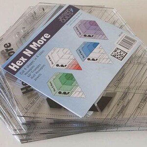 May include: A stack of clear plastic quilting rulers with a blue and white instruction booklet. The booklet is titled "Hex N More" and shows how to cut 4 shapes in 4 sizes: hexagons, 60 triangles, half hexagons, and jewels.