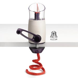 May include: A white and purple yarn winder with a clear plastic top and a red yarn spool. The winder is attached to a table with a clamp. A silver metal bobbin is also visible.