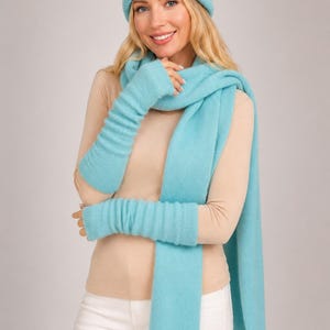 May include: A light blue knit beanie, a matching long knit scarf, and a pair of matching light blue knit arm warmers. The set features a consistent ribbed texture throughout each piece, providing a coordinated look in a soft, bright blue color.