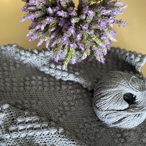 May include: A gray crocheted blanket with a ball of gray yarn and a bouquet of lavender flowers.