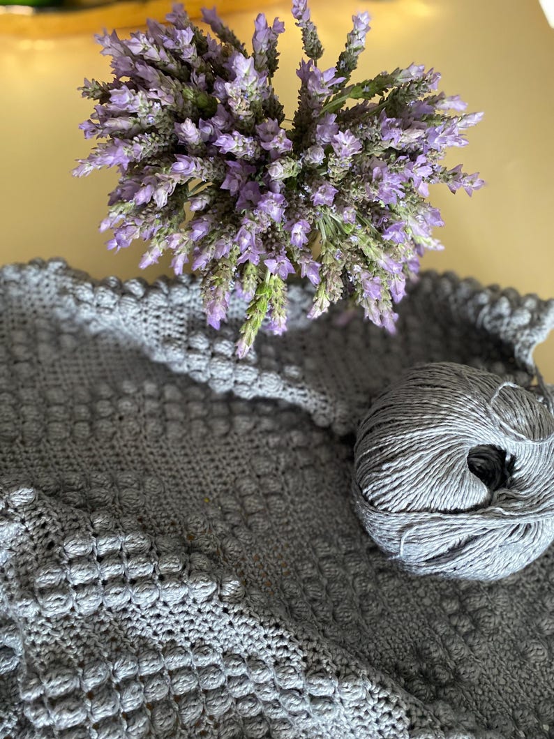 May include: A gray crocheted blanket with a ball of gray yarn and a bouquet of lavender flowers.
