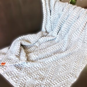 May include: A soft, white crocheted throw blanket with a textured, bobble stitch pattern. The blanket is draped over a brown leather couch.