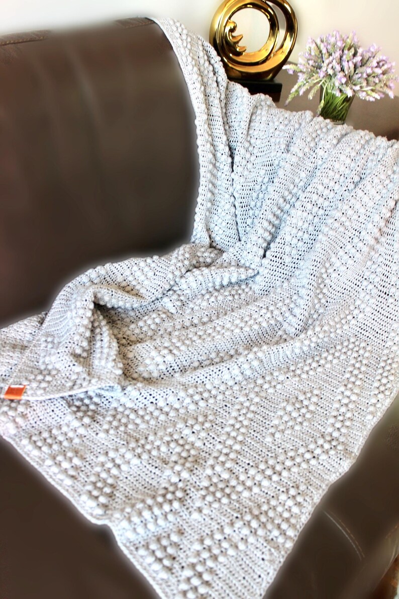 May include: A soft, white crocheted throw blanket with a textured, bobble stitch pattern. The blanket is draped over a brown leather couch.