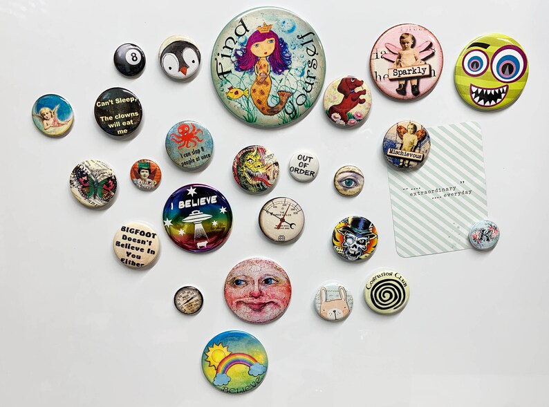 May include: A collection of colorful buttons with various designs and sayings, including "Find Yourself", "I Believe", "Out of Order", "Can't Sleep, The Clowns Will Eat Me", "Bigfoot Doesn't Believe in You Either", "Sparkly", "Mischievous", and "The Conversation Club".