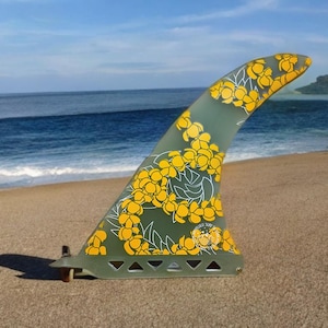 May include: A green surfboard fin with a yellow floral pattern. The fin has a white outline and a logo that says "Surfy Surf".