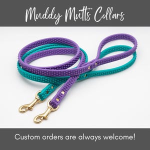 May include: Two dog leashes in teal and purple, with gold-colored clasps. The leashes have a textured, dotted pattern. The text "Muddy Mutts Collars" is at the top, and "Custom orders are always welcome!" is at the bottom.