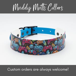 May include: A colorful dog collar with a pattern of video game controllers on a black background. The collar is blue and white with black accents. Muddy Mutts Collars is printed on the top of the image. Custom orders are always welcome! is printed at the bottom of the image.
