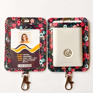 May include: Two rectangular badge holders featuring a dark floral pattern with pink, red, and teal flowers. The left holder displays a sample ID card with a photo and text. The right holder contains a white Centegix device with a circular logo.