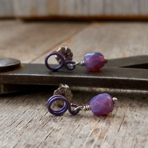 May include: A pair of purple earrings with small, faceted, iridescent purple glass beads and silver wire loops.
