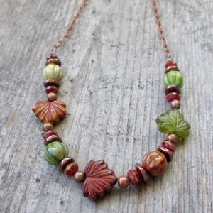 May include: A copper chain necklace with green and red glass beads shaped like leaves. The beads are interspersed with smaller copper beads.