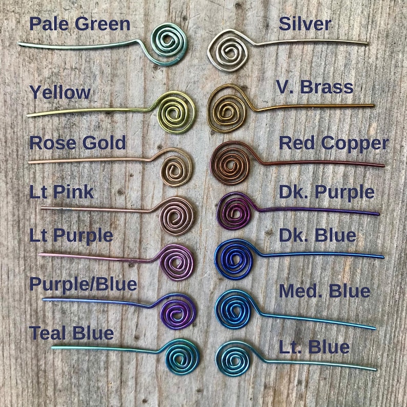 May include: A collection of wire hair pins in various colors, including pale green, silver, yellow, rose gold, and red copper. Each pin features a spiral design at one end and is displayed on a wooden surface.