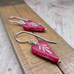 May include: A pair of silver heart-shaped earrings with a red, distressed finish and white etched designs.