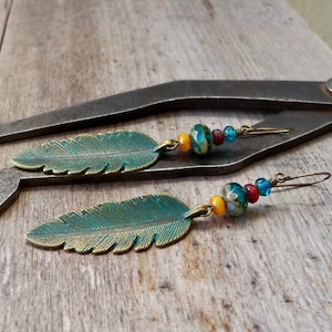 May include: A pair of dangle earrings with turquoise and gold leaf charms. The earrings feature a mix of turquoise, gold, red, and yellow beads.