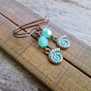 May include: Copper earrings with turquoise blue seashell charms and light green faceted beads.