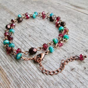 May include: A handmade bracelet featuring a double strand design. The bracelet is made with copper-colored chain and adorned with a variety of colorful beads, including turquoise, burgundy, and brown. The bracelet has a lobster clasp closure.