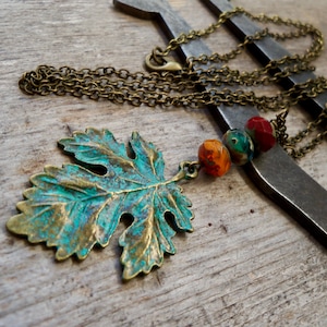 May include: A bronze leaf pendant necklace with turquoise patina and colorful glass beads. The necklace is on a chain with a lobster clasp.