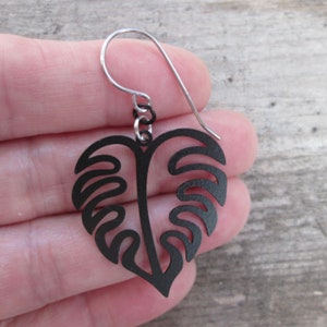 May include: Black metal earrings shaped like a monstera leaf with a silver hook.