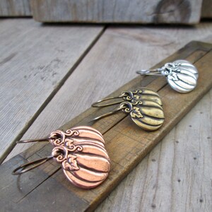 May include: Three pairs of pumpkin-shaped earrings in copper, gold, and silver. Each earring features a detailed design with leaves and swirls.