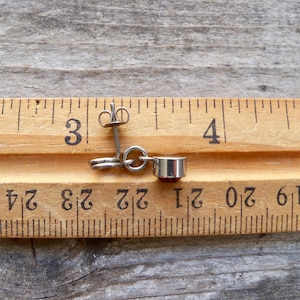 May include: A pair of silver earrings with a red gemstone dangle. The earrings are measured against a wooden ruler, showing they are just over 3 inches long.